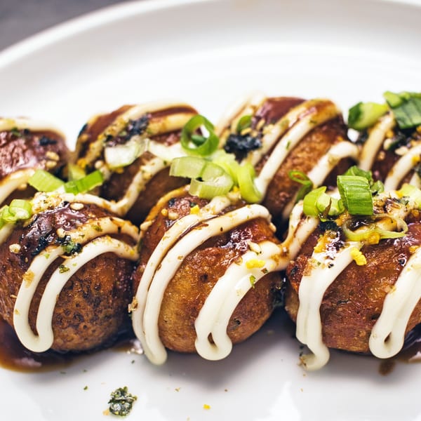 Close-up of Nanabi Cafe's takoyaki, drizzled with white sauce and garnished with green onions.